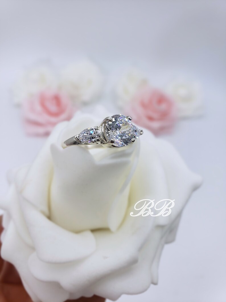 May include: A silver ring with three clear cubic zirconia stones. The center stone is round and the two side stones are pear-shaped.