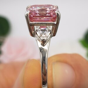Puede incluir: Un anillo plateado con una gran gema rosa rectangular como elemento principal. Una piedra transparente m&aacute;s peque&ntilde;a en forma de coraz&oacute;n est&aacute; engastada debajo de la piedra principal. La banda del anillo es delgada y pulida, con las iniciales "BB" en escritura.