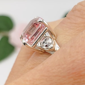 Puede incluir: Un anillo de plata con una gran gema rosa rectangular como pieza central. Dos gemas claras triangulares m&aacute;s peque&ntilde;as flanquean la piedra principal. El anillo tiene un dise&ntilde;o detallado. Las iniciales "BB" est&aacute;n en la parte inferior.