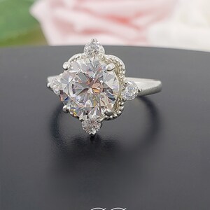 Puede incluir: Un anillo de plata con una gran piedra preciosa redonda y transparente rodeada de piedras preciosas transparentes m&aacute;s peque&ntilde;as. El anillo tiene un dise&ntilde;o delicado y ornamentado.