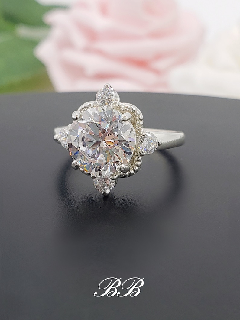 Puede incluir: Un anillo de plata con una gran piedra preciosa redonda y transparente rodeada de piedras preciosas transparentes m&aacute;s peque&ntilde;as. El anillo tiene un dise&ntilde;o delicado y ornamentado.