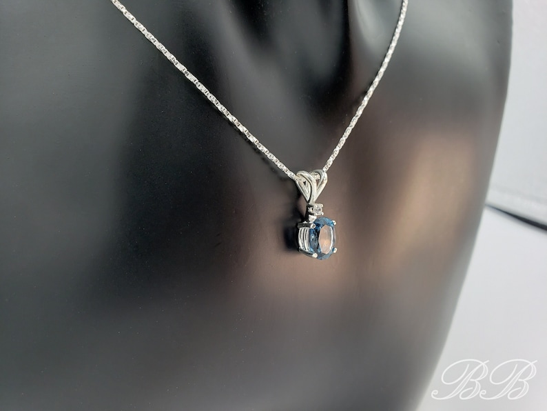 May include: A silver chain necklace with a pendant featuring a blue oval gemstone surrounded by smaller clear gemstones.