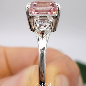 Puede incluir: Un anillo de plata con una gran gema rosa rectangular. Una piedra m&aacute;s peque&ntilde;a, transparente, en forma de coraz&oacute;n est&aacute; engastada debajo de la piedra principal. El anillo tiene una superficie pulida y reflectante. Las iniciales "BB" est&aacute;n en la base del anillo.