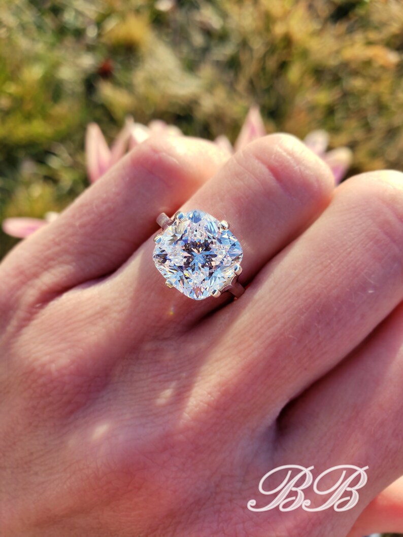 May include: A large, clear, cushion-cut diamond engagement ring set in a silver band.