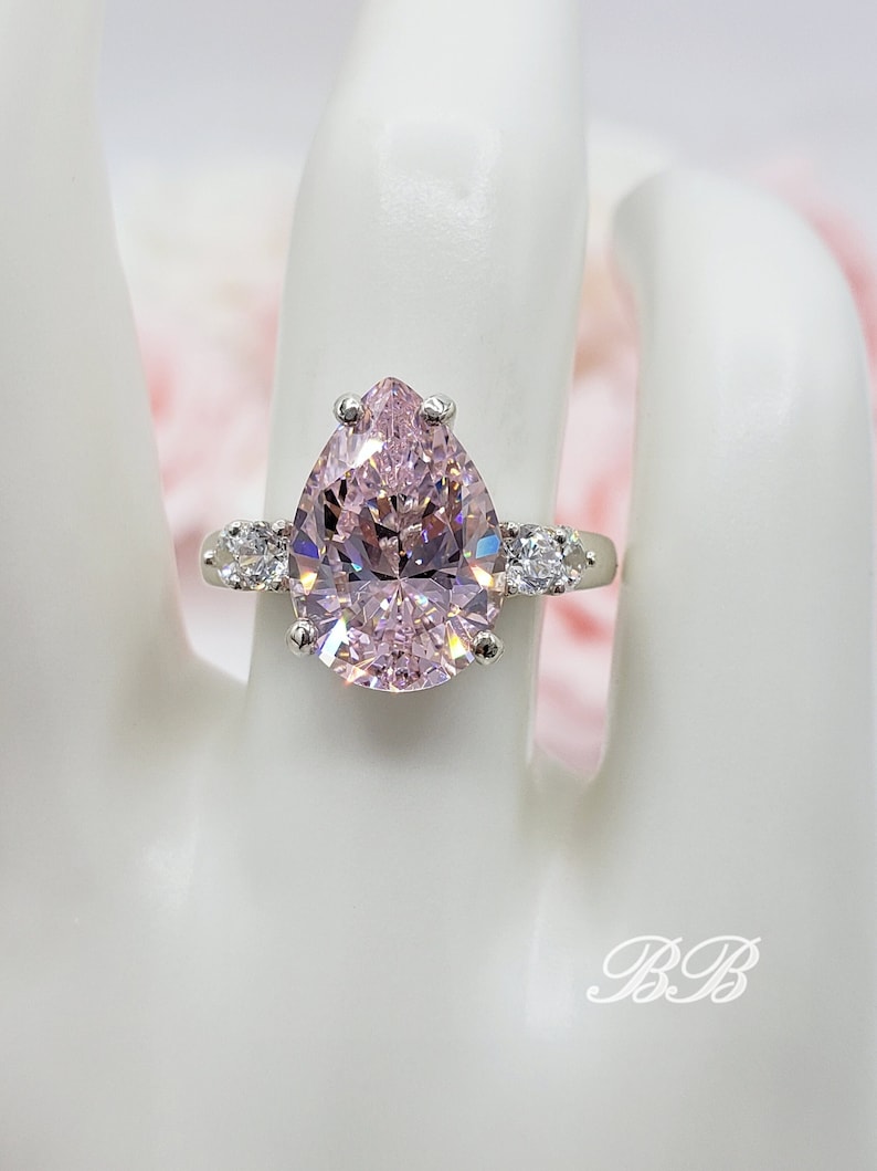 Puede incluir: Un anillo de plata con una piedra preciosa rosa en forma de pera y piedras preciosas m&aacute;s peque&ntilde;as y claras en la banda.