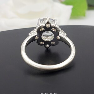 Puede incluir: Un anillo de plata con una gran piedra redonda transparente rodeada de piedras m&aacute;s peque&ntilde;as. El anillo tiene un dise&ntilde;o floral delicado.