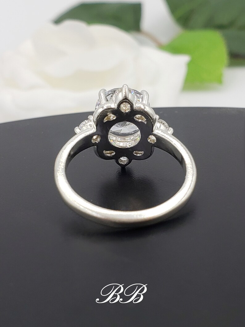 Puede incluir: Un anillo de plata con una gran piedra redonda transparente rodeada de piedras m&aacute;s peque&ntilde;as. El anillo tiene un dise&ntilde;o floral delicado.