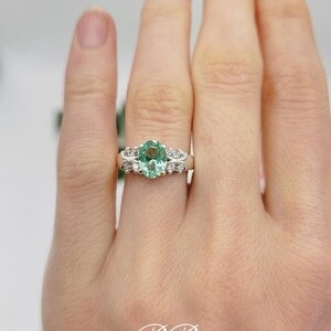 Puede incluir: Un anillo de plata con una gran piedra preciosa ovalada verde rodeada de piedras preciosas m&aacute;s peque&ntilde;as transparentes.