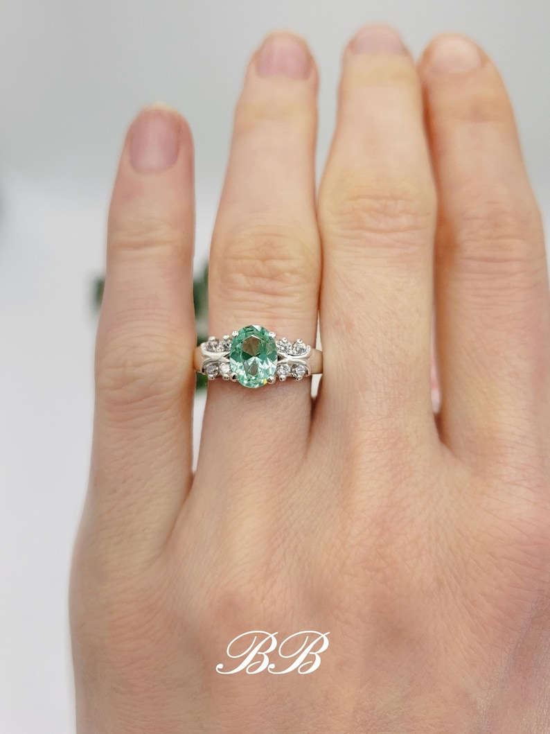 Puede incluir: Un anillo de plata con una gran piedra preciosa ovalada verde rodeada de piedras preciosas m&aacute;s peque&ntilde;as transparentes.