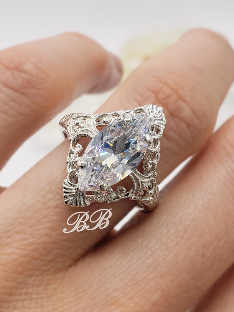 Puede incluir: Un anillo de plata con una piedra grande y transparente de forma marquesa engastada en un dise&ntilde;o de filigrana.