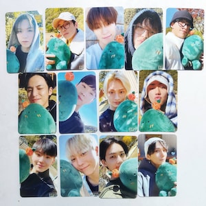 May include: A set of 11 photo cards featuring members of a K-pop group. Each card shows a different member holding a green cactus plush toy. The cards are printed with the group's name, "Seventeen", and the member's name.