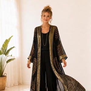 Pode incluir: Um quimono duster longo e transparente em preto com bordados dourados metálicos em padrões de folhas e chevron. A peça possui mangas largas, um acabamento preto sólido ao longo da abertura frontal e um design fluido e aberto.