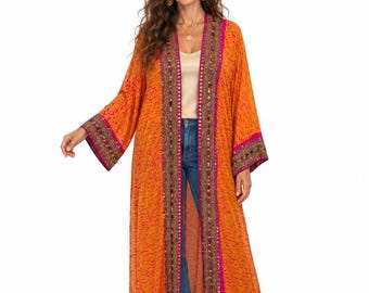 May include: A long, open-front orange kimono featuring a textured pattern, wide sleeves, and a decorative border in magenta and metallic gold with intricate embroidery and small mirror accents along the front opening and sleeve cuffs.