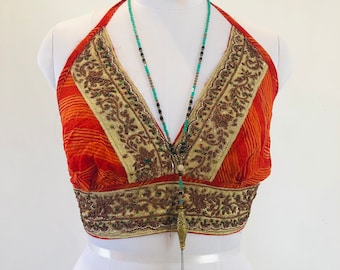 May include: An orange halter top with gold and brown embroidery and a turquoise and black beaded necklace with a teal tassel. The top is displayed on a white mannequin.