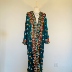 Könnte beinhalten: Ein langer, blaugrüner, durchsichtiger Kimono mit goldenen und roten Stickereien. Der Kimono hat einen tiefen V-Ausschnitt und lange Ärmel.