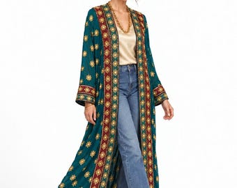 May include: A long, teal duster coat featuring intricate gold floral embroidery and a wide, dark red border with geometric patterns. The garment is worn over a champagne-colored satin camisole, blue denim jeans, and black pointed-toe ankle boots.