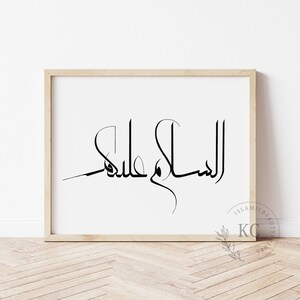 May include: A framed print with the Arabic calligraphy "Assalamu Alaikum" in black ink on a white background. The frame is light wood.