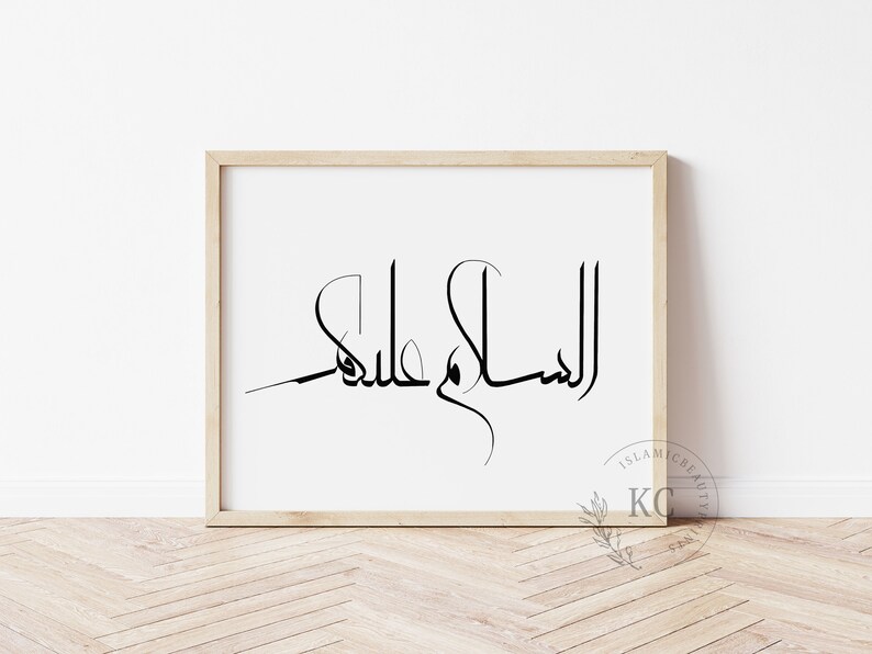 May include: A framed print with the Arabic calligraphy "Assalamu Alaikum" in black ink on a white background. The frame is light wood.