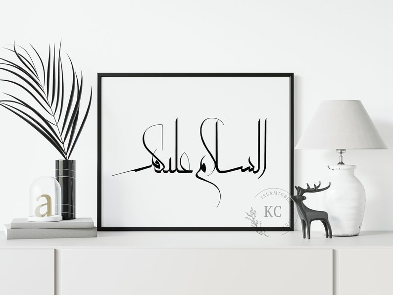 May include: Black and white calligraphy print with the Arabic phrase "Al Salam Alaykum" in a modern style. The print is framed in a black frame and is hanging on a white wall.