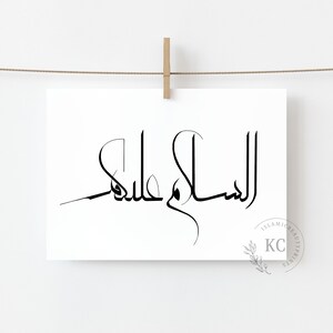 May include: A black and white print of the Arabic phrase "Assalamu Alaikum" meaning "Peace be upon you" in a modern calligraphy style. The print is hanging on a white wall with a wooden clothespin.