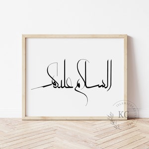 May include: A framed print with the Arabic calligraphy "Assalamu Alaikum" in black ink on a white background. The frame is light wood.