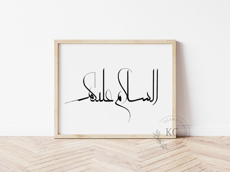 May include: A framed print with the Arabic calligraphy "Assalamu Alaikum" in black ink on a white background. The frame is light wood.