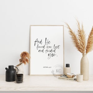 May include: A framed print with a black and white calligraphy quote that reads "And He found you lost and guided you." The quote is from the Islamic scripture Ad-Duha, 9:17. The print is on a white background and has a light wood frame.