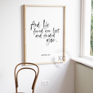 May include: A framed print with a white background and black calligraphy that reads "And He found you lost and guided you." The text is attributed to Ad-Duba, 93:7. The print is framed in a light wood frame.
