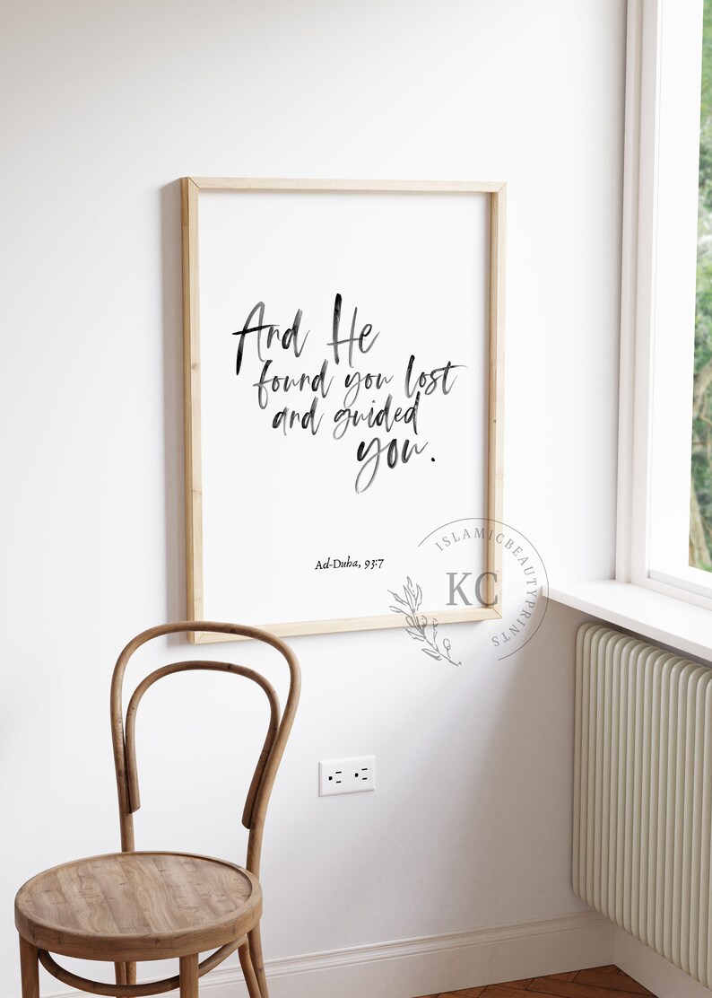 May include: A framed print with a white background and black calligraphy that reads "And He found you lost and guided you." The text is attributed to Ad-Duba, 93:7. The print is framed in a light wood frame.