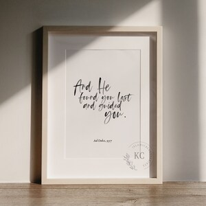 May include: A framed print with a white background and black calligraphy that reads "And He found you lost and guided you." The text is attributed to Ad-Duba, 93:7. A small logo with the letters "KC" and a branch of leaves is in the bottom right corner.