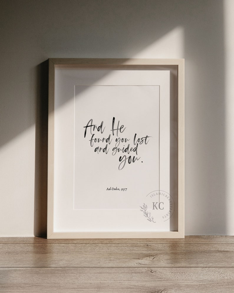 May include: A framed print with a white background and black calligraphy that reads "And He found you lost and guided you." The text is attributed to Ad-Duba, 93:7. A small logo with the letters "KC" and a branch of leaves is in the bottom right corner.