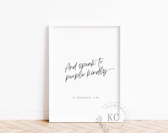 May include: White framed print with the text "And speak to people kindly" in elegant black script. Below the text is "AL-BAQARAH, 2:83". The print is leaning against a white wall on a light wood floor.