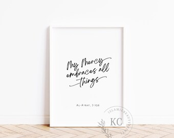 May include: White framed print with the text "My Mercy embraces all things" in elegant black script. The print also includes the text "AL-A'RAF, 7:156" and a logo. The artwork is displayed against a white wall and wooden floor.