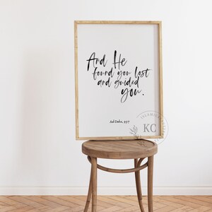 May include: A framed print with a white background and black calligraphy text that reads "And He found you lost and guided you." The text is followed by "Ad-Duba, 93:7" and a logo that reads "ISLAMIC FAMILY KC" in a black and white font.