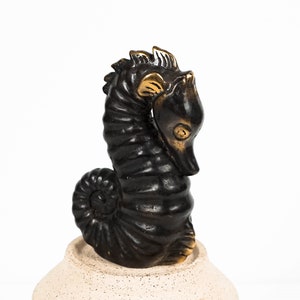 May include: A black and gold seahorse figurine with a detailed, textured surface. The seahorse is curled up in a sitting position.