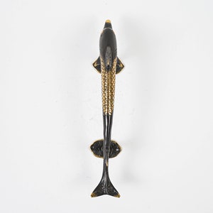 May include: A decorative door handle in the shape of a fish. The handle is black with gold accents, including the scales, fins, and tail. The handle is mounted on a decorative base.