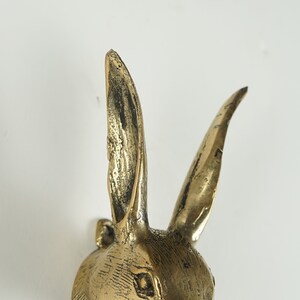 Peut inclure: Une figurine de t&ecirc;te de lapin en m&eacute;tal couleur laiton avec de longues oreilles dress&eacute;es et une finition textur&eacute;e et patin&eacute;e. La sculpture pr&eacute;sente des lignes grav&eacute;es d&eacute;taill&eacute;es repr&eacute;sentant la fourrure et un &oelig;il d&eacute;fini sur la partie sup&eacute;rieure.