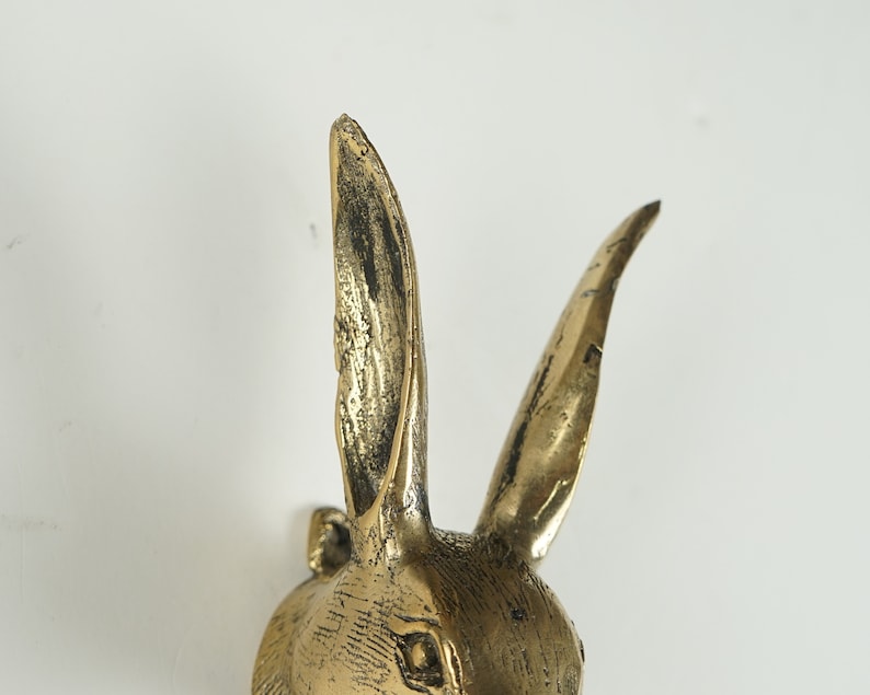 Peut inclure: Une figurine de t&ecirc;te de lapin en m&eacute;tal couleur laiton avec de longues oreilles dress&eacute;es et une finition textur&eacute;e et patin&eacute;e. La sculpture pr&eacute;sente des lignes grav&eacute;es d&eacute;taill&eacute;es repr&eacute;sentant la fourrure et un &oelig;il d&eacute;fini sur la partie sup&eacute;rieure.
