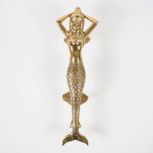 May include: A gold-toned mermaid door knocker with a shell on her head and a detailed fishtail.