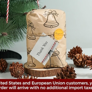 May include: A rectangular package wrapped in brown paper featuring a black line-art bell pattern. The package is tied with twine, secured with a round yellow sticker, and includes a white tag with the printed text Thank You in black ink.