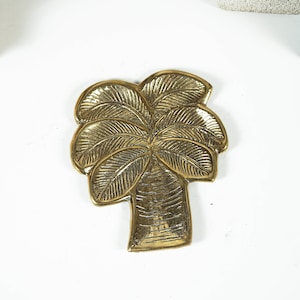 Może przedstawiać: Złota, metalowa tacka w kształcie palmy. Tacka ma szczegółowy wzór.