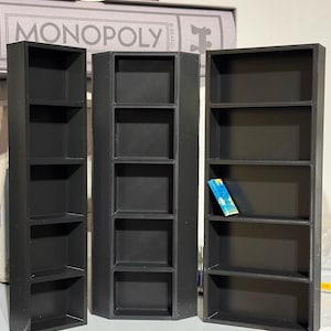 May include: Three black, rectangular, open-shelf storage units with five shelves each. The units are made of a textured plastic material. The middle unit is slightly angled. A small blue and white card is on the top shelf of the rightmost unit.
