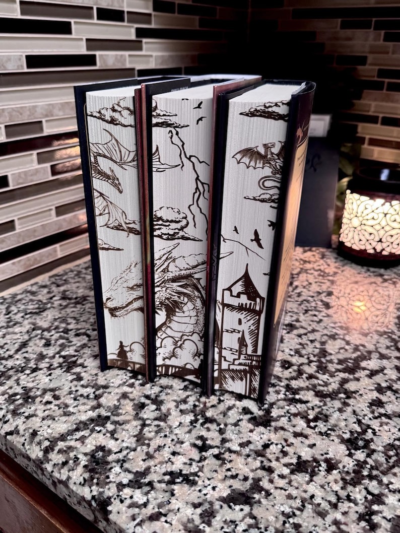 May include: Three hardback books with white covers and brown illustrations of dragons, clouds, and a castle. The books are arranged vertically, with the tallest book on the right.