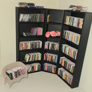 Könnte beinhalten: Ein schwarzes Bücherregal mit mehreren Regalbrettern, die mit bunten Büchern gefüllt sind. Das Bücherregal steht in einer Ecke eines Raumes und hat einen kleinen weißen Korbstuhl mit Büchern darauf.