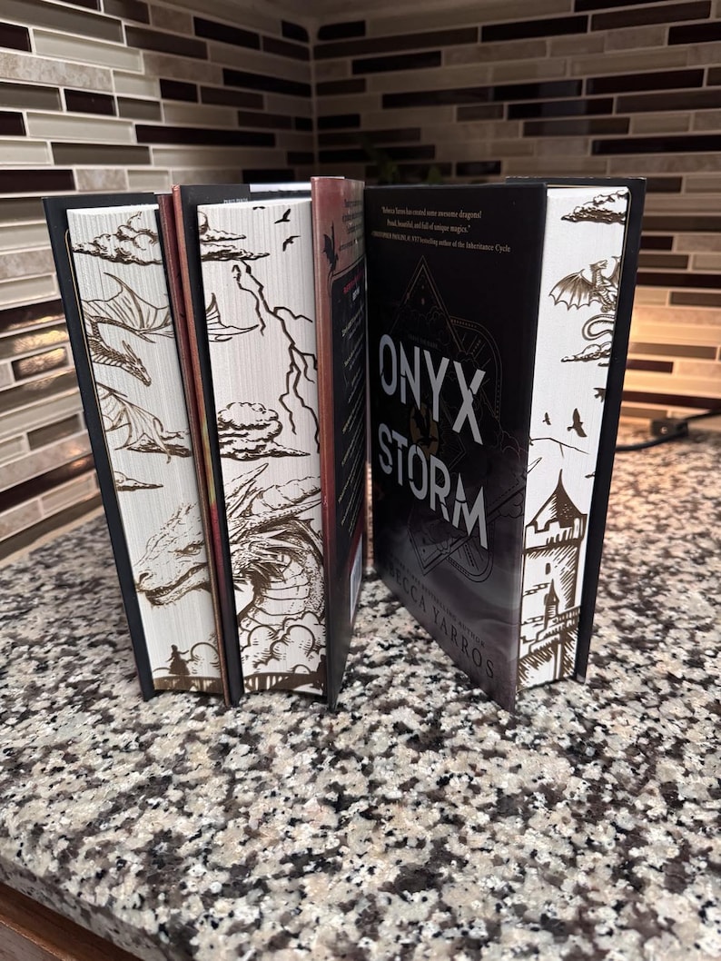 May include: A set of five fantasy novels with black spines and white covers featuring dragon and castle illustrations. The title of the centre book is "ONYX STORM" by Rebecca Yarros.