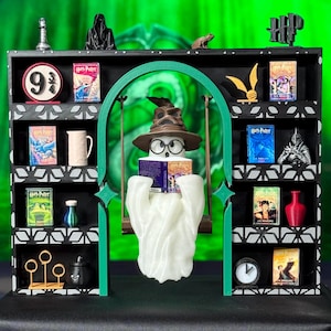May include: A black and white shelf unit with a green archway, featuring miniature Harry Potter-themed items. Includes books, a ghost figure wearing a Sorting Hat, and other decorative elements. The background is a vibrant green.
