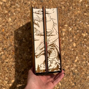 May include: Two hardback books with brown and white illustrated covers featuring a dragon and clouds. The books are bound in black with gold accents.