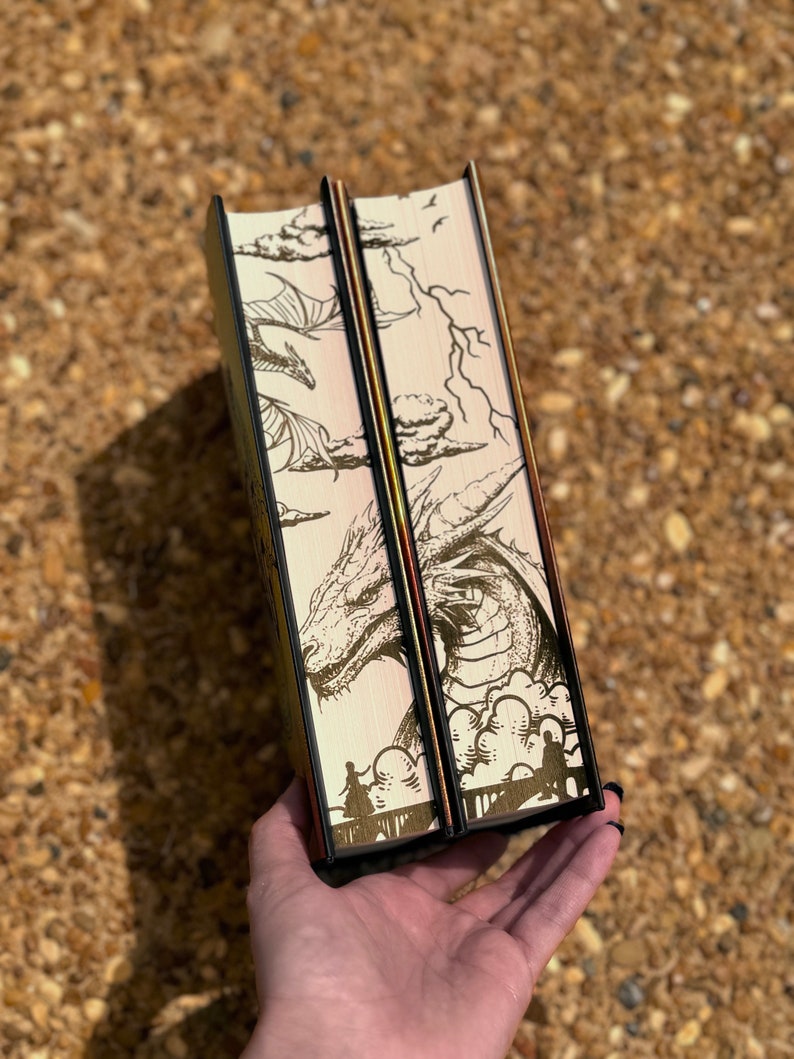 May include: Two hardback books with black spines and gold accents. The covers feature a detailed illustration of a dragon with clouds and lightning in the background.