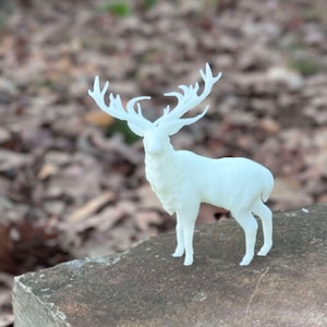 May include: A white 3D printed deer figurine with large antlers. The deer is standing on a brown rock.