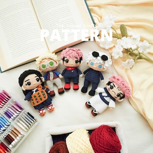 May include: A collection of six handmade crochet dolls with detailed facial features and unique outfits. The dolls are arranged on a cream-colored surface, with a partially visible open book and the word "PATTERN" in white text.